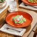 A table with two Acopa Keystone Sedona Orange porcelain coupe plates of food on it.