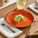 An Acopa Sedona Orange porcelain coupe plate with food on a table.