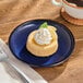 A small round blue porcelain coupe plate holding a dessert with whipped cream and fruit garnish.