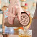 A man using a Barfly copper-plated Hawthorne strainer to pour a drink into a glass.