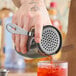 A hand using a Barfly gun metal black Hawthorne strainer to pour a drink into a glass.