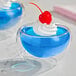 A glass cup with blue JELL-O and a cherry on top.