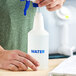 A plastic spray bottle labeled 'WATER' being assembled by a person.