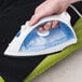 A hand using a Hamilton Beach white non-stick hospitality iron on a green pillow.