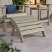A Lancaster Table & Seating gray Adirondack footrest on a wooden patio table.