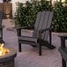 A black Lancaster Table & Seating modern Adirondack chair on a brick patio next to a fire pit.