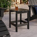 A black Lancaster Table & Seating Adirondack side table on an outdoor patio with a drink on it.