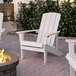 A white Lancaster Table & Seating modern Adirondack chair sits next to a fire pit.