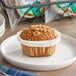 A single coffee cake muffin in a white paper liner on a white plate.