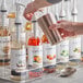 A person pouring Capora Peach Flavoring Syrup into a glass.
