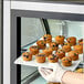 A person holding a tray of Abe's Vegan Wild Blueberry Mini Muffins on a counter in a bakery display.