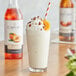 A glass of milkshake with whipped cream and peaches made with Capora Peach Flavoring Syrup.