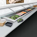 A Hatco drop-in refrigerated cold food well with two slanted pans holding food on a counter in a display case.