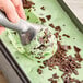 A hand scooping G.S. Gelato Mint Chocolaty Gelato with a metal scoop.