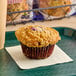 An individually wrapped blueberry crumb muffin on a tray.