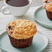 A David's Cookies Blueberry Crumb Muffin on a plate next to a cup of coffee.