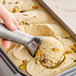 A hand scooping G.S. Gelato Sicilian Pistachio gelato with a metal scoop.
