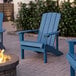 Two blue Lancaster Table & Seating Modern Adirondack chairs on a brick patio next to a fire pit.