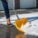 A person using a True Temper yellow snow shovel with snow on the street.