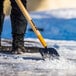 A person using a True Temper sidewalk scraper to remove snow.