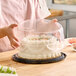 A woman holding a cake in a Baker's Lane plastic display container with a clear scalloped dome lid.