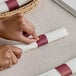 A person's hands wrapping a piece of paper with a burgundy self-adhering band.