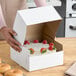 A woman opening a Baker's Lane white cake box to reveal a cake with strawberries on top.