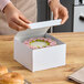 A person opening a Baker's Lane white bakery box with a donut inside.