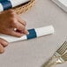 A hand using a knife to cut a blue paper napkin band.