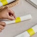 A hand wrapping a white napkin with a yellow Choice paper napkin band.