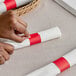 A person's hands using red self-adhering paper to wrap a white napkin.