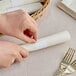 A hand using a white Choice paper napkin band to wrap a napkin around a fork.