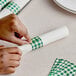 A person's hands wrapping a napkin with green and white checkered paper tape.