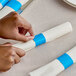 A person's hands using a Choice blue self-adhering paper napkin band to wrap a white fabric napkin.