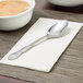 A Oneida Rosewood stainless steel oval bowl soup spoon on a napkin next to a bowl of soup.