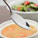 A Oneida Rosewood stainless steel oval bowl spoon over a bowl of soup.