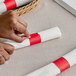 A person's hands wrapping a white napkin with a red Choice paper band.