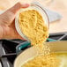 A hand pouring Knorr Caldo de Pollo chicken bouillon powder into a pot of food.