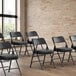 A row of Lancaster Table & Seating black folding chairs with black cushions in a room.