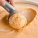 A hand scooping orange ice cream from a container.