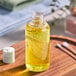 A 4 oz. PET clear Boston round bottle of yellow liquid on a wooden tray next to cotton buds and a white container with a handle.
