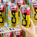 A 16 fl. oz. can of C4 Energy Hawaiian Punch Fruit Juicy Red energy drink being held in front of several identical cans on a refrigerator shelf.