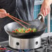 A 16-inch oxidized carbon steel Mandarin wok being used to stir-fry vegetables on a stovetop.
