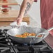 A person cooking noodles and vegetables in an Emperor's Select Cantonese Wok on a gas stove.