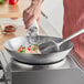 A person cooking food in an Emperor's Select carbon steel wok.