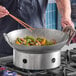 A 16-inch carbon steel Cantonese wok being used to stir-fry vegetables on a stovetop.