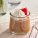 A glass jar of chocolate pudding with whipped cream and a raspberry on top.