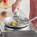 A person cooking vegetables in an Emperor's Select carbon steel wok on a stove.
