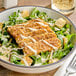 A bowl of salad with tempeh, meat, and cheese on top.
