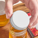 A person holding a 43/400 white metal lid on a jar of honey.